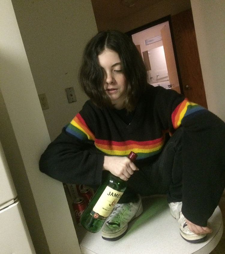 girl in a rainbow sweater, bottle of Jameson, squatting on top of a round table.